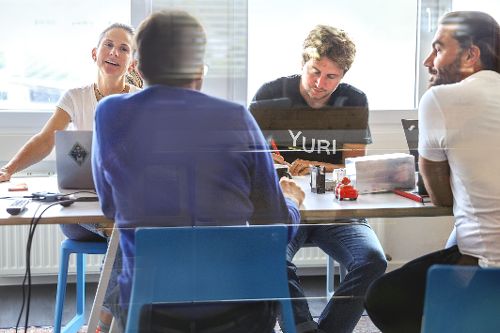 Vier Personen sitzen an einem Tisch in einem Besprechungsraum und arbeiten gemeinsam an Laptops.