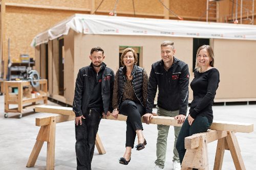 Vier Personen stehen in einer Produktionshalle und posieren gemeinsam an einer Holztraverse.