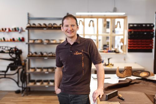Person steht in einer Werkstatt neben einem Arbeitstisch mit Ledermaterialien und Werkzeugen