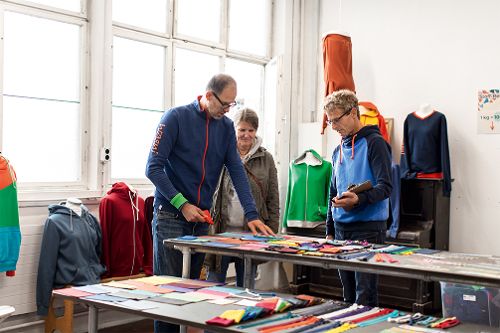 Mehrere Personen betrachten verschiedene Stoff- und Materialmuster, die auf Tischen in einem Ausstellungs- oder Arbeitsraum ausgelegt sind.