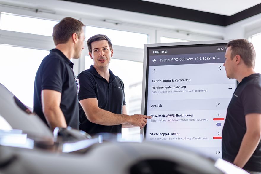 Drei Personen besprechen Testergebnisse an einem großen digitalen Display.