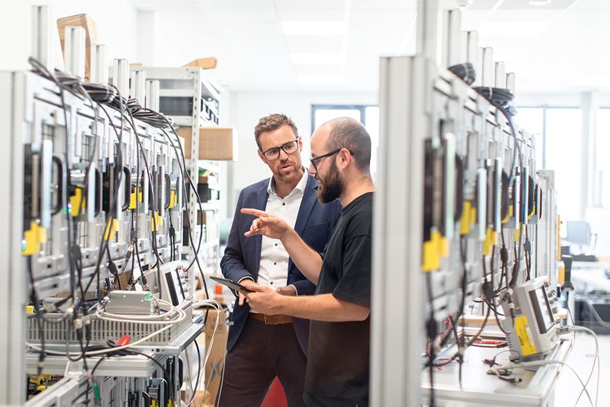Zwei Personen prüfen technische Geräte in einer Produktions- oder Testumgebung.