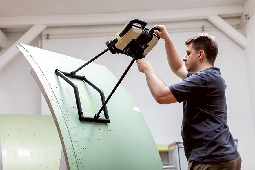 Person arbeitet mit einem mobilen Messgerät an einem Flugzeugbauteil in einer technischen Entwicklungsumgebung.