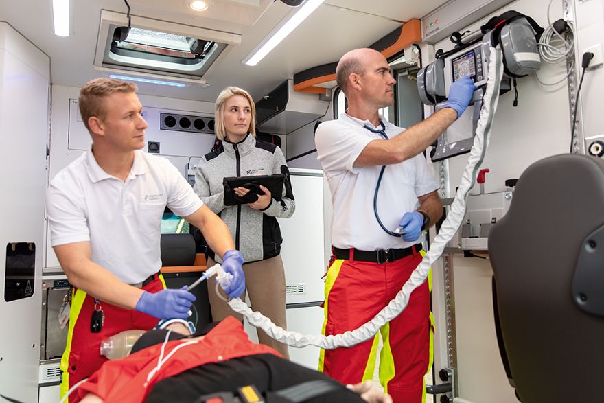 Drei Personen arbeiten in einem Rettungsfahrzeug mit medizinischer Ausstattung.