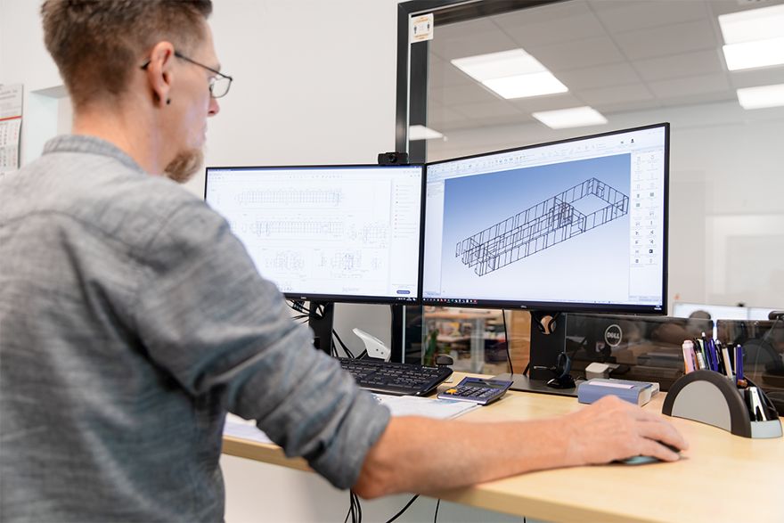 Person arbeitet an einem Computerarbeitsplatz mit zwei Monitoren und erstellt oder bearbeitet ein digitales 3D-Modell in einer Konstruktions- oder Entwicklungsumgebung.