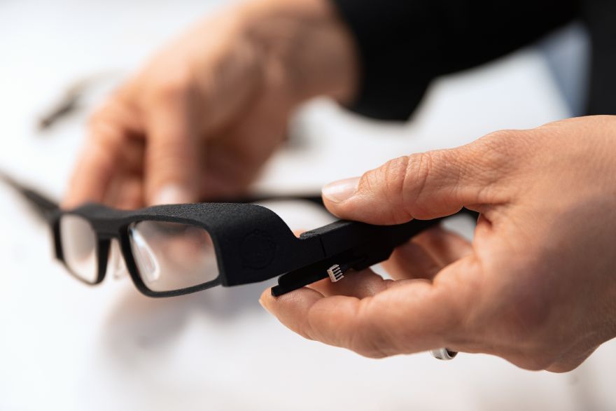 Nahaufnahme einer intelligenten Brille, die von einer Person in den Händen gehalten wird. Die Brille verfügt über integrierte elektronische Komponenten und Sensoren im Bügelbereich.