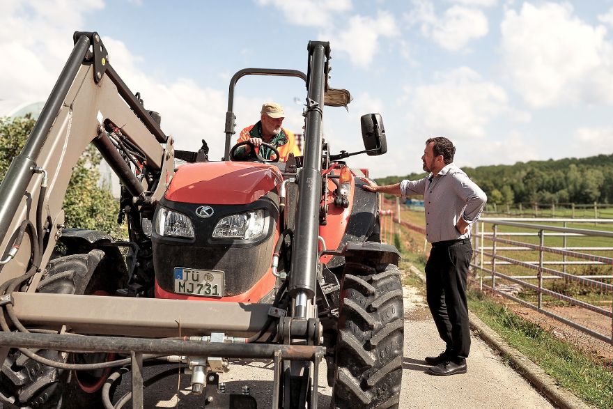 Eine Person sitzt in einem großen Traktor und unterhält sich mit einer Person, die neben dem Traktor steht.