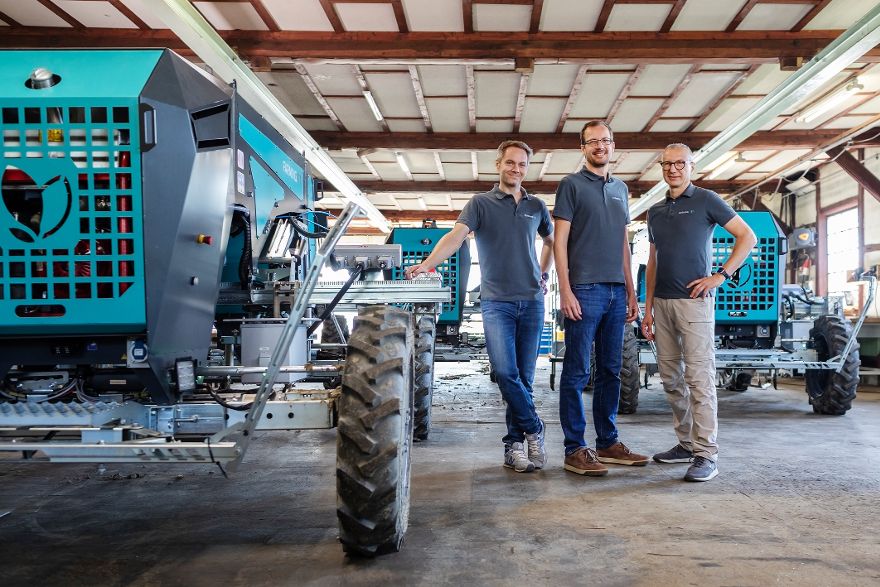 Drei Männer stehen neben großen landwirtschaftlichen Maschinen.