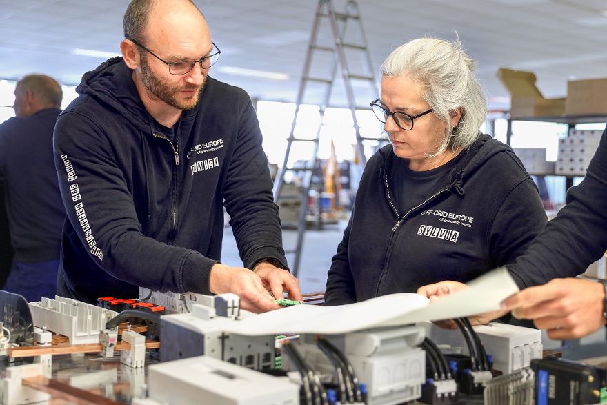 Zwei Personen arbeiten gemeinsam an einer elektrischen Anlage auf einem Arbeitstisch.