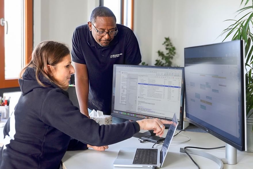Zwei Personen arbeiten an einem Schreibtisch mit Laptop und zwei Monitoren und analysieren gemeinsam Inhalte auf den Bildschirmen.