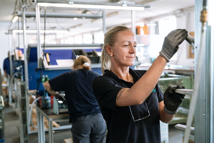 Person montiert ein Bauteil an einer Fertigungsstation in einer Produktionshalle.