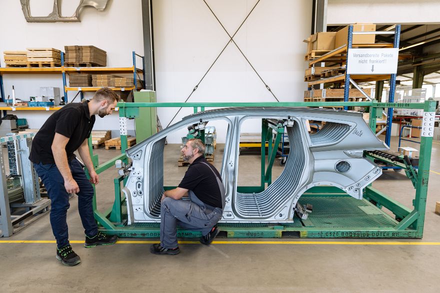 Zwei Personen arbeiten in einer Produktionshalle an einer großen Metallstruktur.