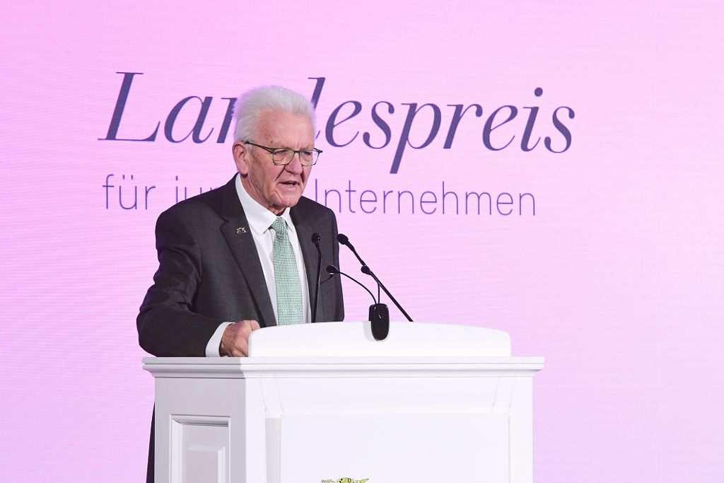 Winfried Kretschmann steht auf Landespreis-Bühne hinter einem Pult mit Mikrofon.