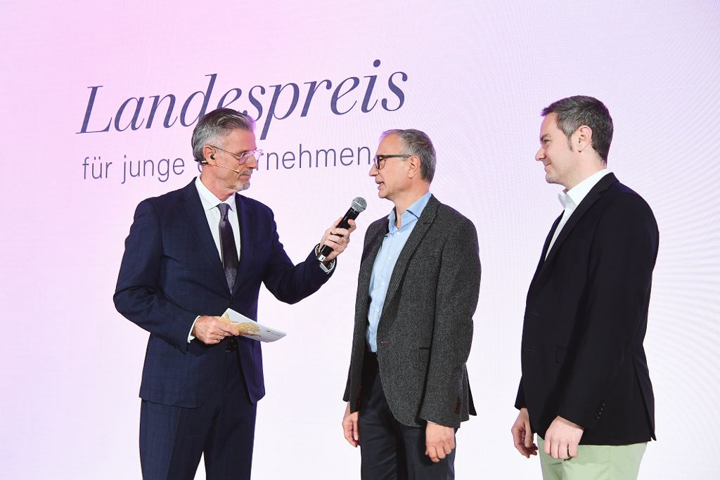 Ein Mann interviewt zwei Männer auf der Bühne der Landespreis-Preisverleihung.
