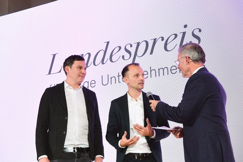 Ein Mann interviewt zwei Männer auf der Bühne der Landespreis-Preisverleihung.