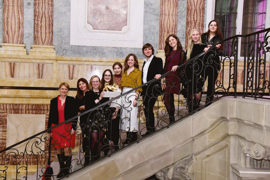 Gruppenfoto mehrerer Personen auf einer repräsentativen Treppe in einem historischen Gebäude. Einige halten eine Auszeichnung in den Händen.