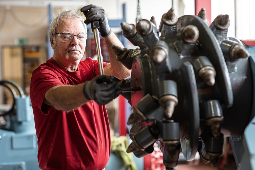 Person arbeitet mit einem Spezialwerkzeug an einer großen Fräsmaschine in einer Werkhalle.