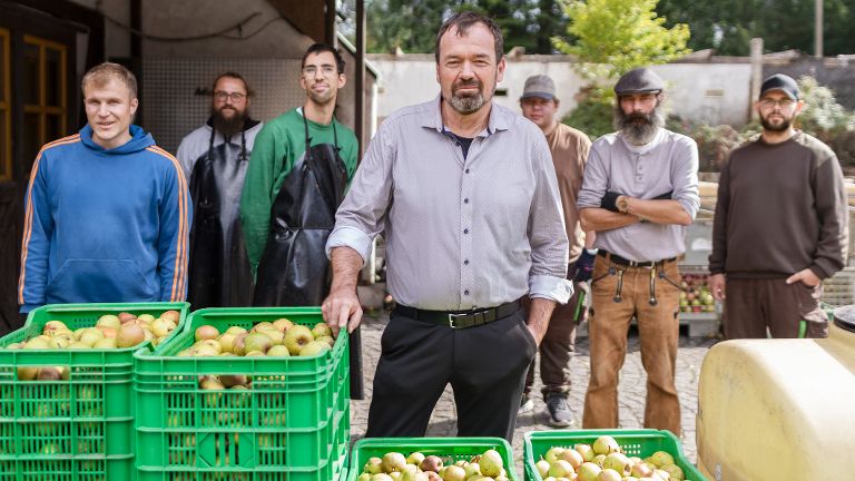 Mehrere Personen stehen im Freien hinter grünen Kisten mit Obst.